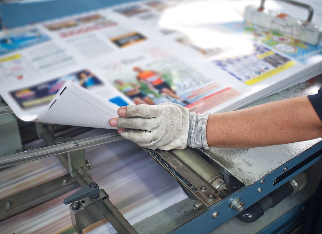 Photography Industry Insurance - Close Up of Person Printing Magazines with a Glove on Their Hand While They Work on the Press